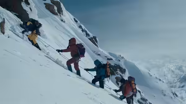A rope team climbs diagonally across a steep, snow-covered mountainside