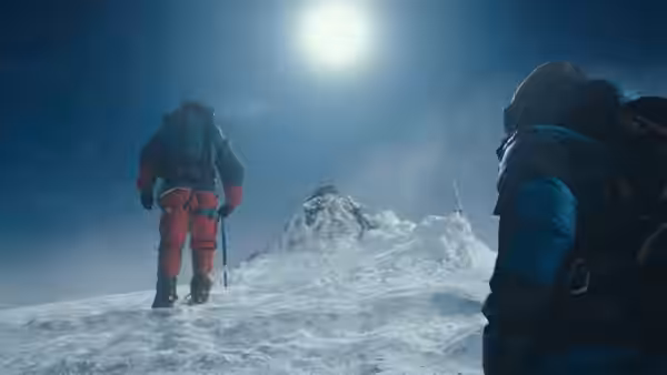 A mountaineer pauses on a snowy ridge beneath the bright sun as another approaches
