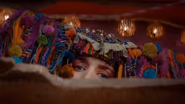 A boy peers over a ledge beneath an elaborate feathered headdress