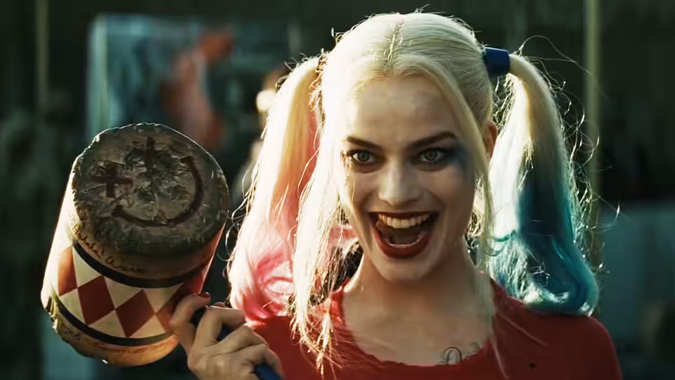 Harley Quinn (Margot Robbie) grins while holding a bloodied wooden mallet