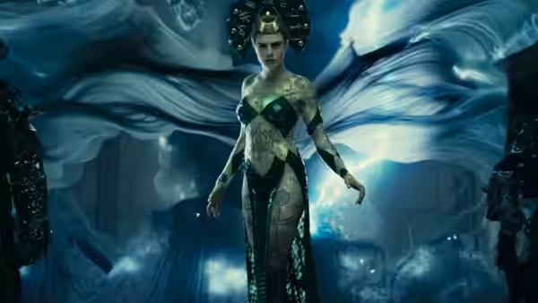 Enchantress (Cara Delevingne) stands amid flowing blue fabric in a dark, cavernous chamber