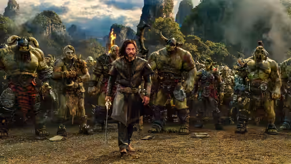 Anduin Lothar (Travis Fimmel) walks among a group of orc warriors in a mountain valley