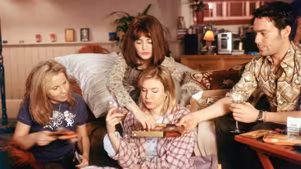 Bridget Jones's friends gather around her on a sofa as a man offers her food