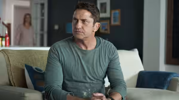 Mike Banning (Gerard Butler) sits on a sofa while a woman stands behind him