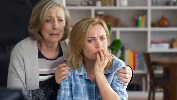 A woman comforts a younger woman as they watch anxiously from a home