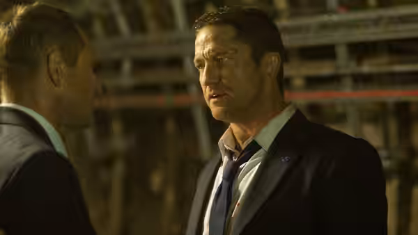 Mike Banning (Gerard Butler) speaks with a man inside a dim industrial structure