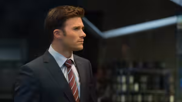 A suited man in a striped tie stands inside a modern building