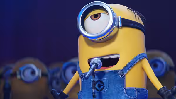 A one-eyed Minion speaks into a microphone as others gather behind him