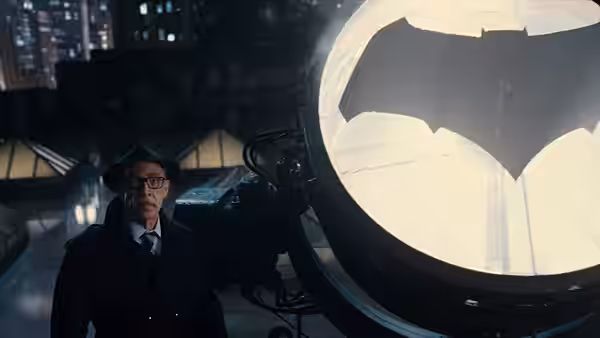 Alfred stands beside a glowing Bat-Signal on a rooftop at night