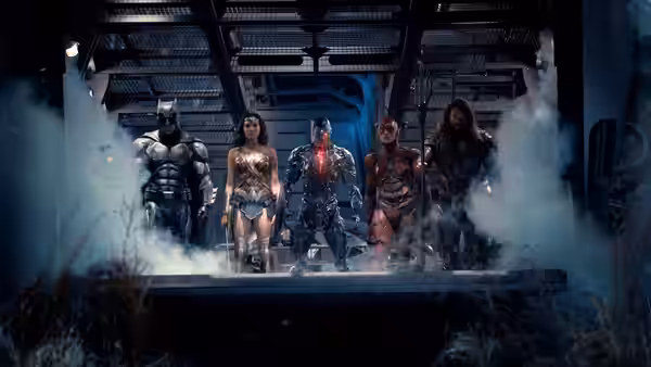 Batman, Wonder Woman, Cyborg, the Flash, and Aquaman emerge through smoke inside a metal hangar