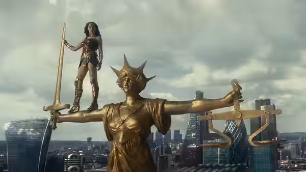 Wonder Woman stands atop a gilded statue above a city skyline