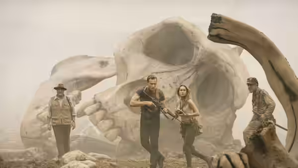 Captain James Conrad and Mason Weaver cross a rocky clearing before a giant skull