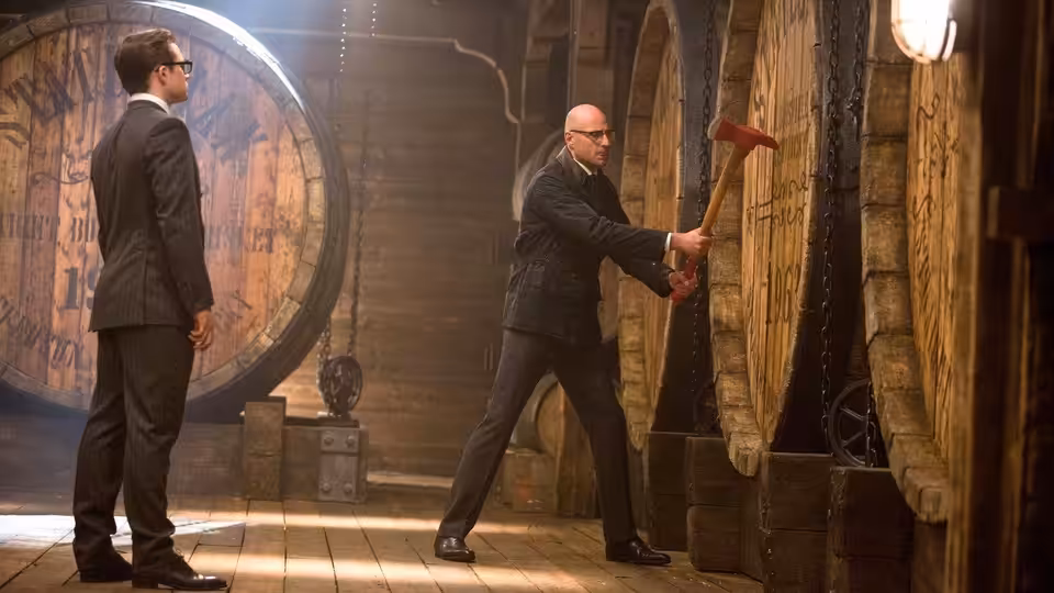 A suited man watches as another swings an axe at a wooden barrel in a cellar