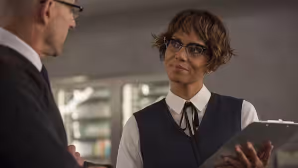 Ginger (Halle Berry) holds a tablet while speaking with a bespectacled man
