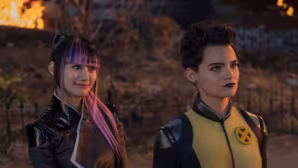 Negasonic Teenage Warhead and a purple-haired woman stand outdoors near flames