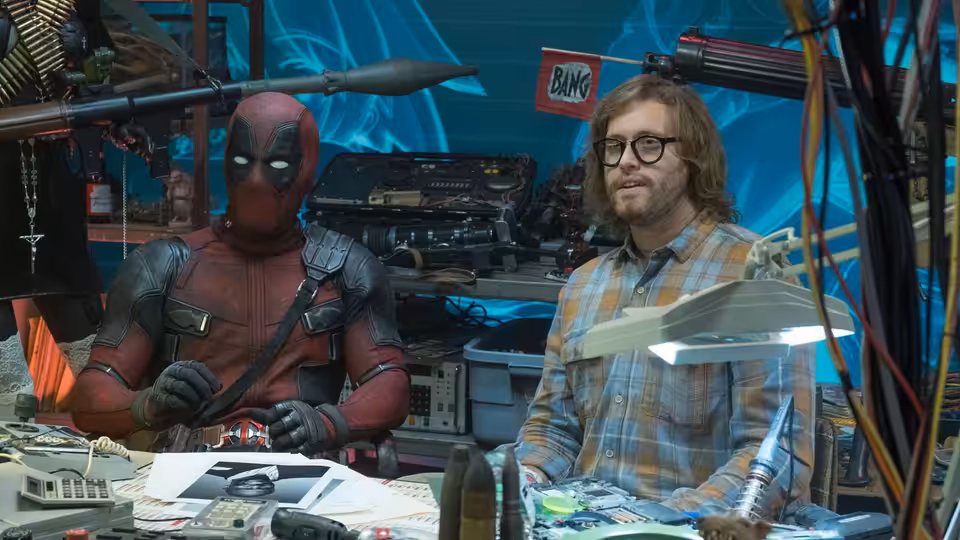 Deadpool and Weasel sit together at a cluttered workbench surrounded by equipment