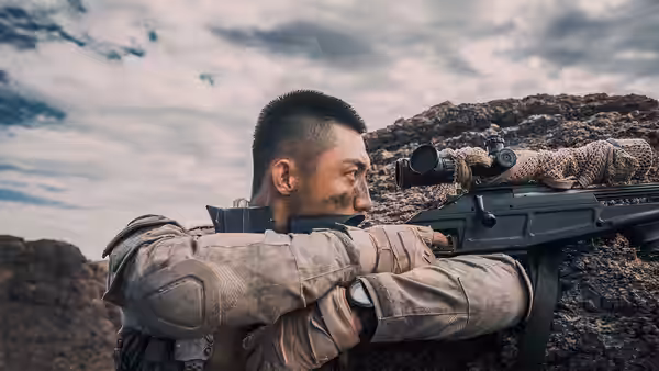 A soldier aims a scoped rifle from behind a rocky ridge