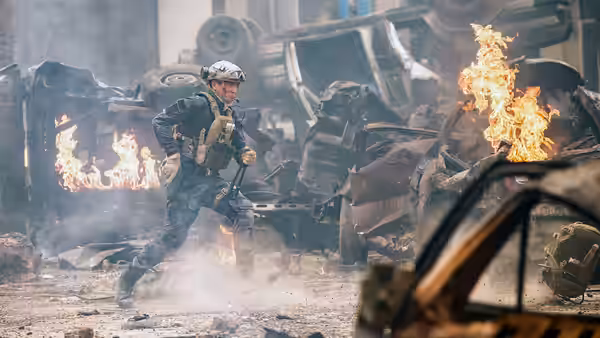 A soldier moves through burning wreckage and smoke amid overturned vehicles