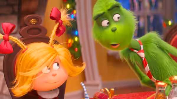 The Grinch leans toward Cindy-Lou Who beside a festively decorated table
