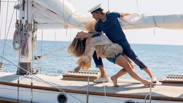 Young Donna (Lily James) and a man dance on the deck of a sailboat
