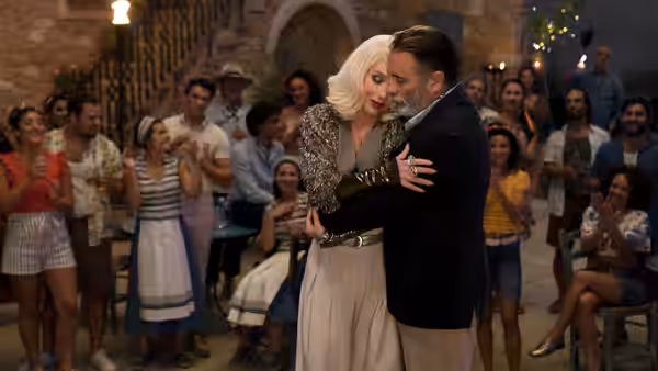 A blonde woman and a man embrace as villagers gather around them