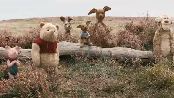 Winnie the Pooh, Piglet, Tigger, and other toy animals gather around a fallen log