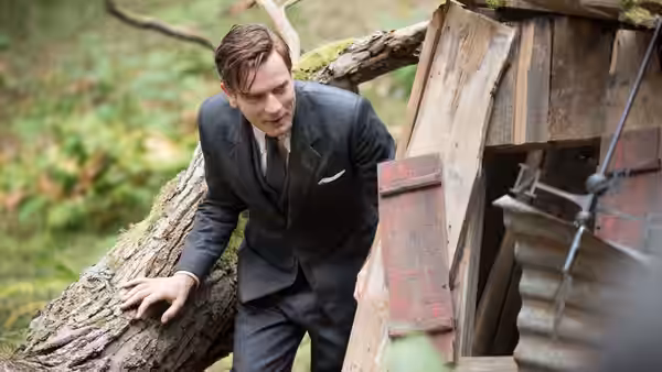 Christopher Robin leans beside a hollow tree in the woods