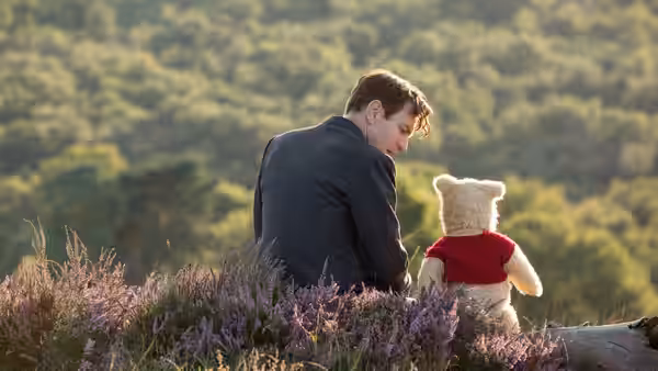 Christopher Robin sits beside Winnie the Pooh among purple heather