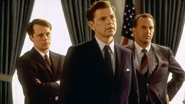 Kenneth O'Donnell (Kevin Costner) stands before the American flag with two suited men