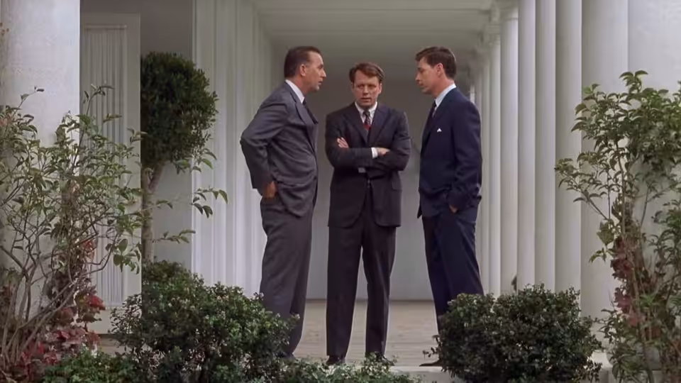 Kenneth O'Donnell (Kevin Costner) talks with two men beneath the White House colonnade