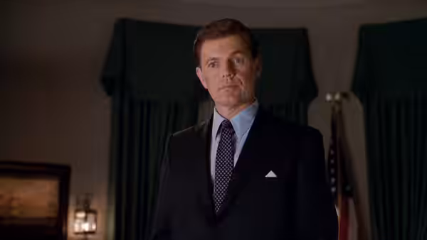 Kenneth O'Donnell (Kevin Costner) stands alone beside a window and American flag