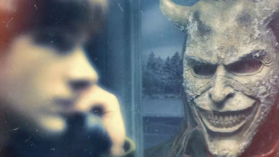 Finn (Mason Thames) holds a phone while facing a horned masked figure at the window