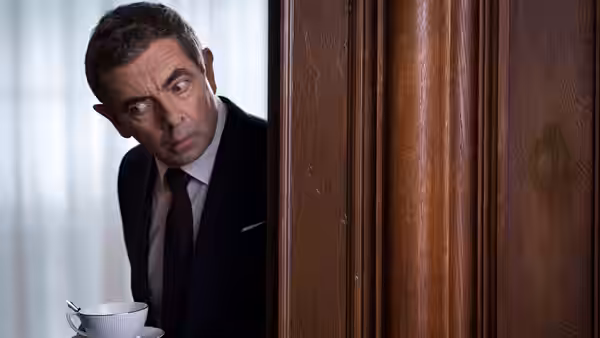 Johnny English (Rowan Atkinson) peeks around a doorway while holding a cup