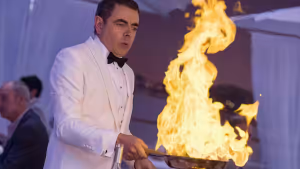 Johnny English (Rowan Atkinson) flambés food in a pan at a formal dinner