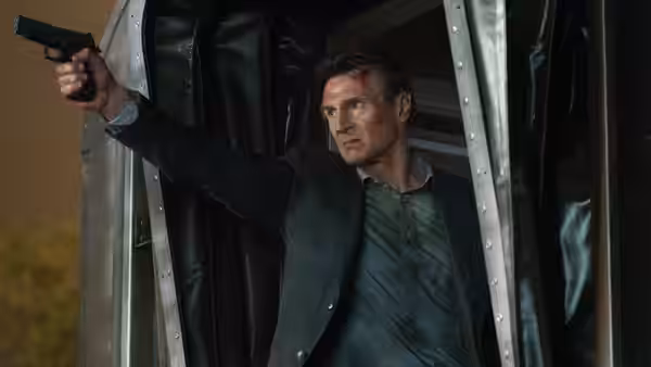 Michael MacCauley (Liam Neeson) aims a pistol from behind a train curtain