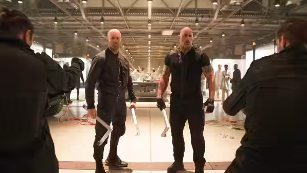 Luke Hobbs (Dwayne Johnson) and Deckard Shaw (Jason Statham) advance with weapons through a warehouse