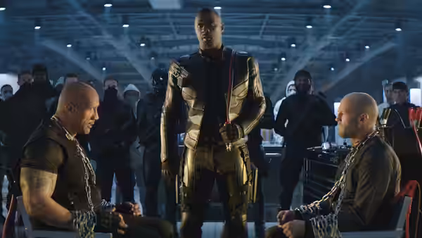 Brixton (Idris Elba) stands between seated Luke Hobbs (Dwayne Johnson) and Deckard Shaw (Jason Statham)