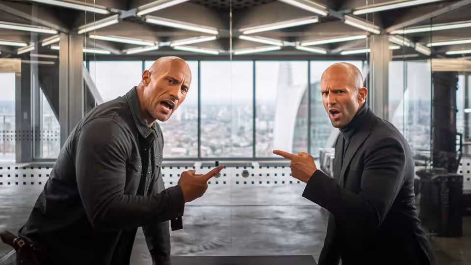 Luke Hobbs (Dwayne Johnson) and Deckard Shaw (Jason Statham) point at each other in an office