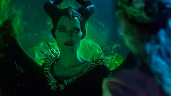 Maleficent (Angelina Jolie) stands amid glowing green magic, her wings framing her