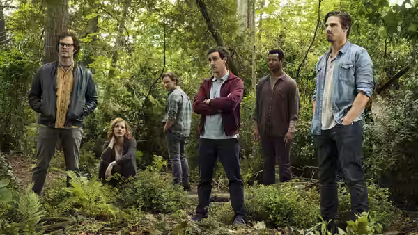 The adult Losers’ Club gathers among trees in the woods