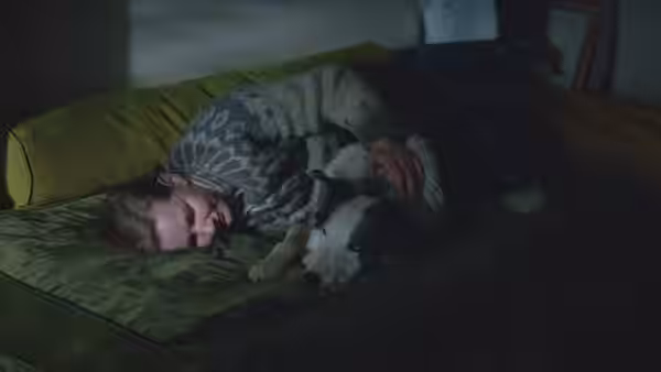 Sandra Voyter lies on a couch cuddling a dog in a dim room