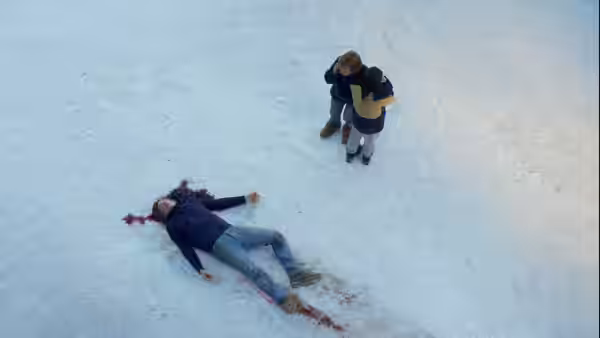 A body lies bleeding in the snow while a person stands nearby