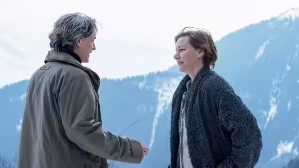 Sandra Voyter and a man face each other outdoors near mountains