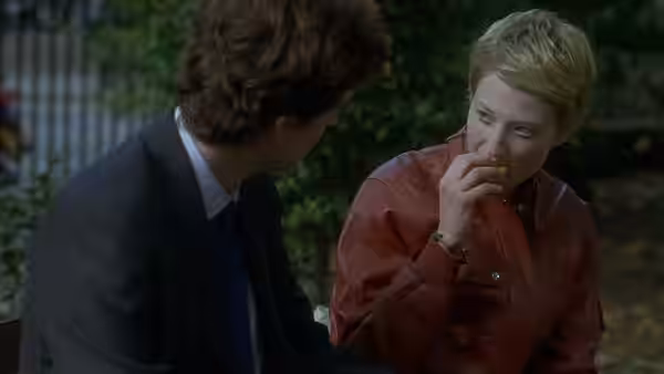 Elisabetta Recchi (Alba Rohrwacher) sits outdoors beside a suited man, eating a small bite