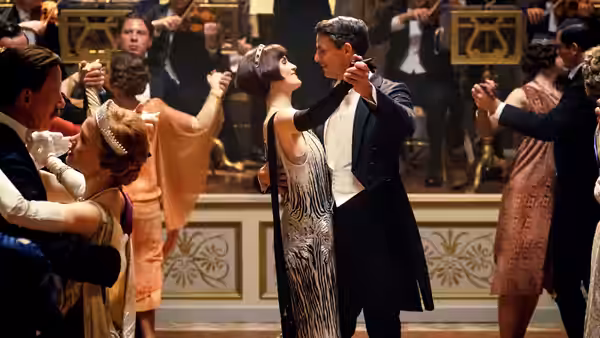A formally dressed couple dance among guests at a crowded ballroom celebration