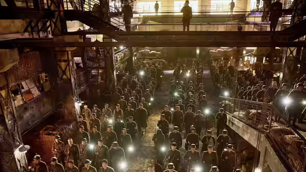 Chinese soldiers crowd a dim warehouse beneath a lone figure on an overhead walkway