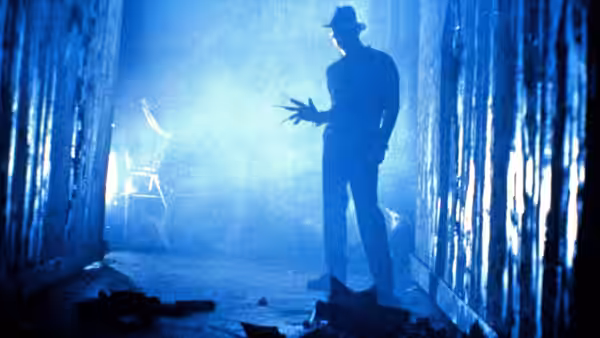 Fred Krueger (Robert Englund) gesturing inside a smoky blue corridor