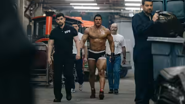 Mark Kerr (Dwayne Johnson) walks shirtless through a garage surrounded by staff and vehicles