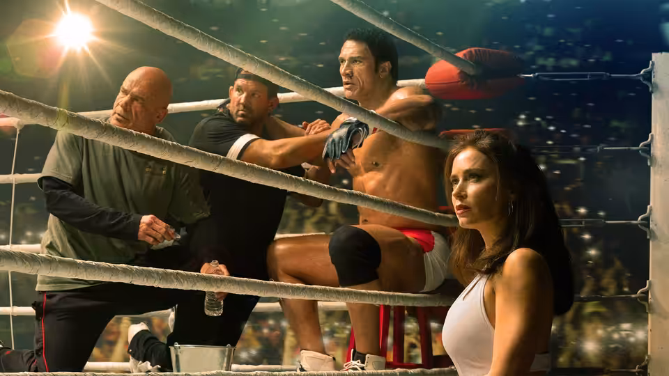 Mark Kerr (Dwayne Johnson) climbs the ropes in a boxing ring while Dawn Staples (Emily Blunt) watches