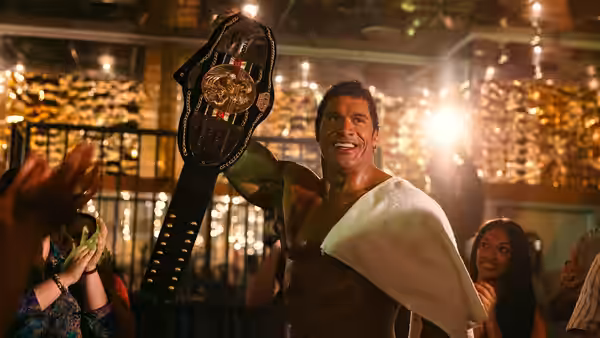 Mark Kerr (Dwayne Johnson) raises a championship belt and smiles inside a crowded venue